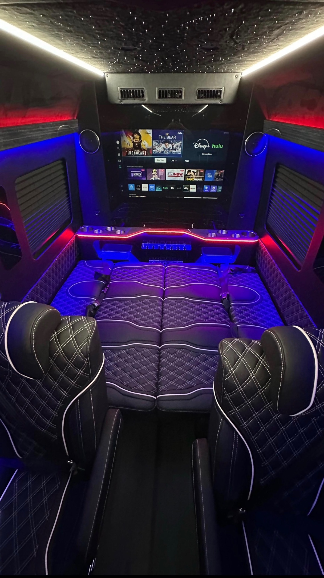 Black leather seats folded into a bed under blue and red lighting with a starlit ceiling