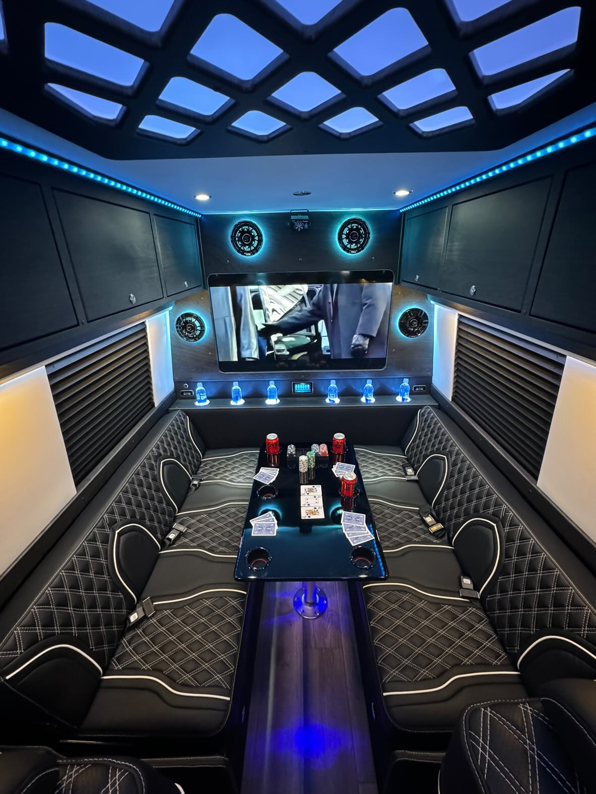 Limo bus lounge with U-shaped black leather seating, white diamond stitching and a gaming table