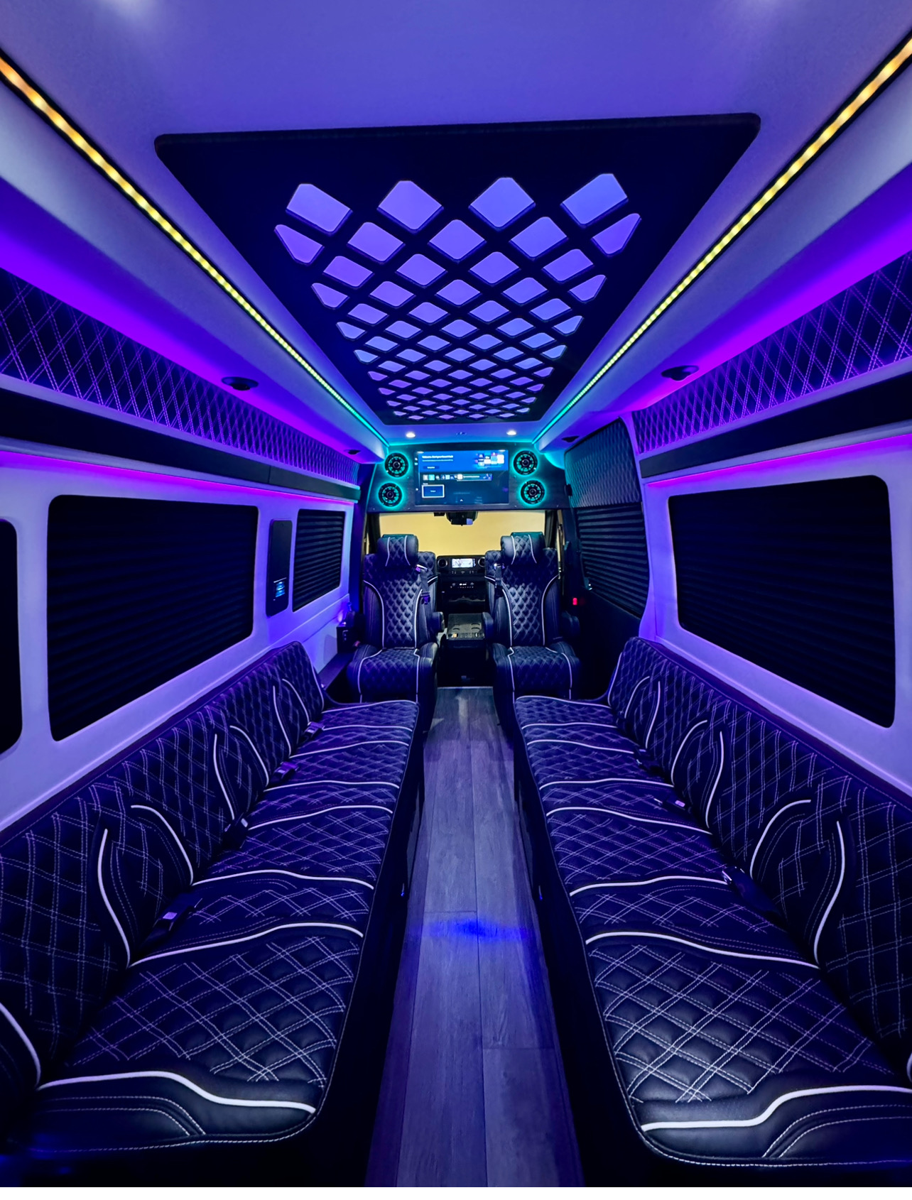 Black leather perimeter benches and captain chairs with white diamond stitching under purple and teal LEDs