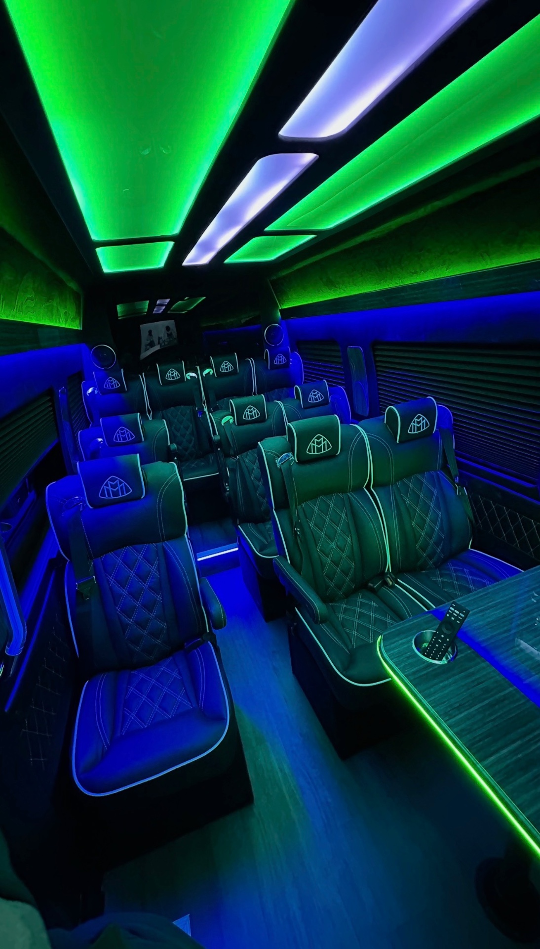 Sprinter cabin with rows of black diamond-quilted seats under neon blue and green lighting